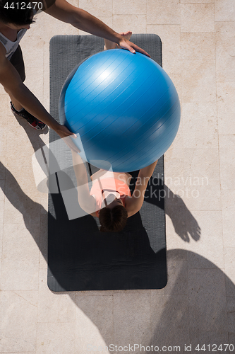 Image of woman and personal trainer doing exercise with pilates ball