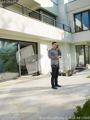 Image of man using mobile phone in front of his luxury home villa