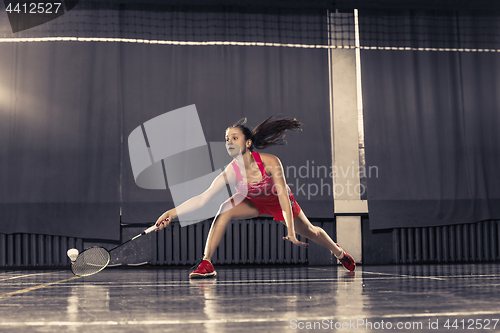 Image of Young woman playing badminton at gym