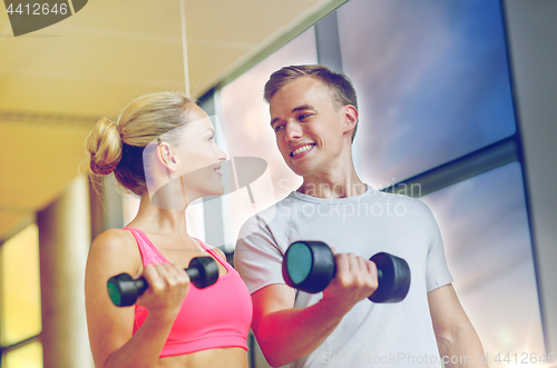 Image of smiling young woman with personal trainer in gym