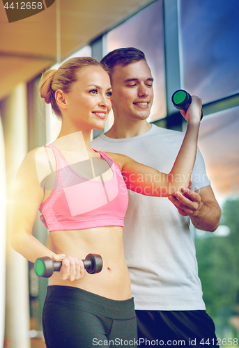 Image of smiling young woman with personal trainer in gym