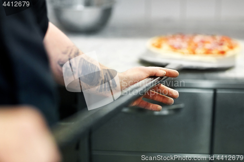 Image of cook or baker hand with pizza on peel at pizzeria