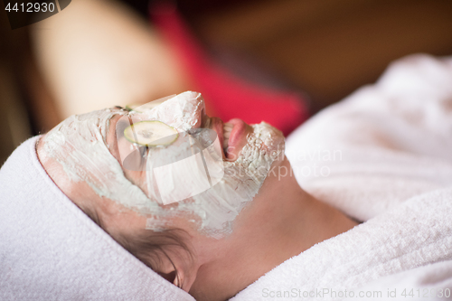 Image of woman is getting facial clay mask at spa