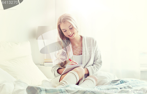 Image of happy young woman with notebook in bed at home