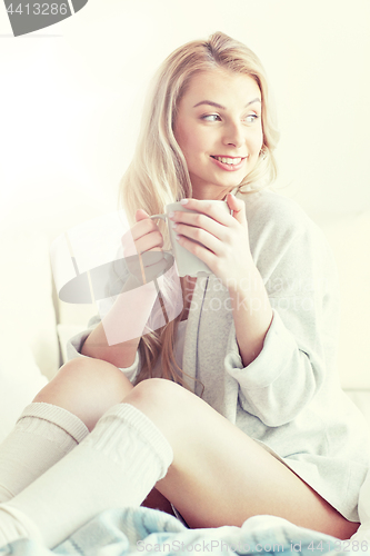 Image of happy woman with cup of coffee in bed at home