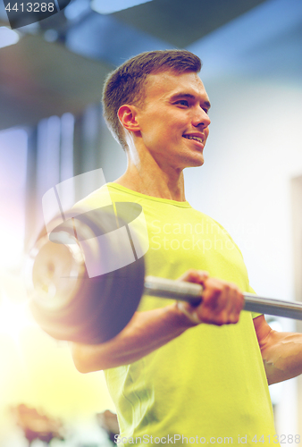 Image of smiling man doing exercise with barbell in gym