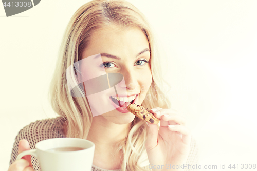 Image of happy woman with tea eating cookie at home