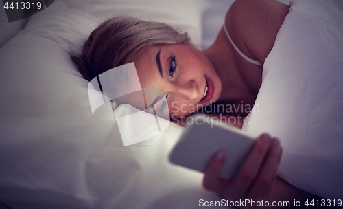 Image of young woman with smartphone in bed at home bedroom