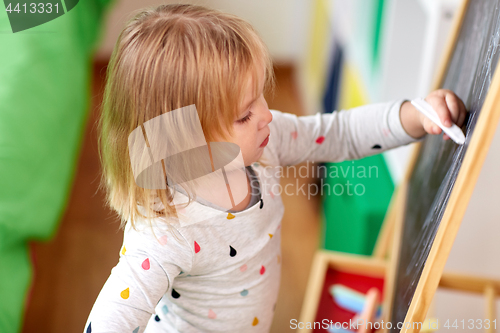 Image of happy little girl drawing on chalk board at home