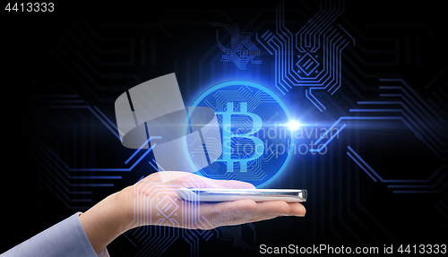 Image of close up of hand with smartphone and bitcoin