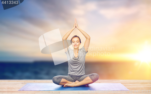 Image of woman meditating in lotus pose on mat outdoors