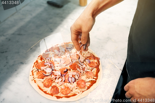 Image of cook adding onion to salami pizza at pizzeria