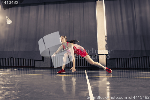 Image of Young woman playing badminton at gym