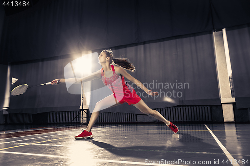 Image of Young woman playing badminton at gym