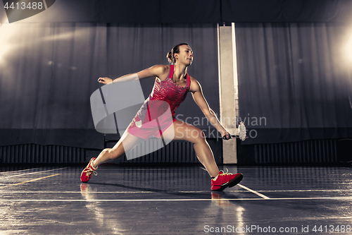 Image of Young woman playing badminton at gym