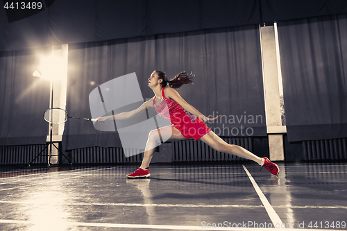 Image of Young woman playing badminton at gym