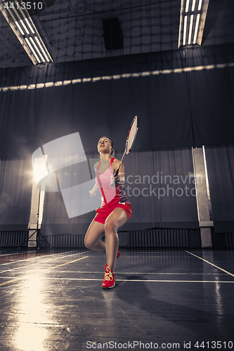 Image of Young woman playing badminton at gym