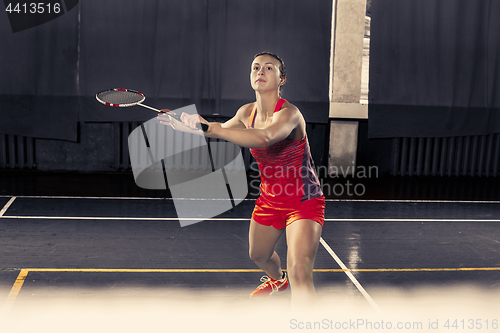 Image of Young woman playing badminton at gym