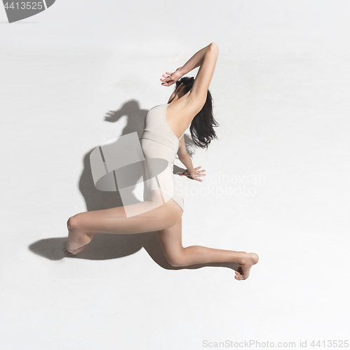 Image of Young beautiful dancer in beige dress dancing on gray background