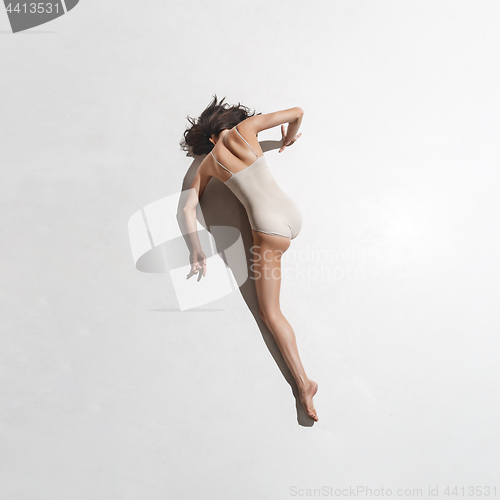 Image of Young beautiful dancer in beige dress dancing on gray background