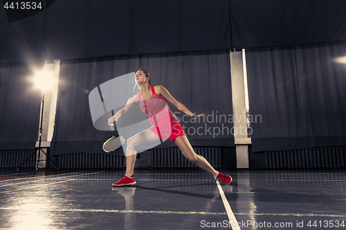 Image of Young woman playing badminton at gym