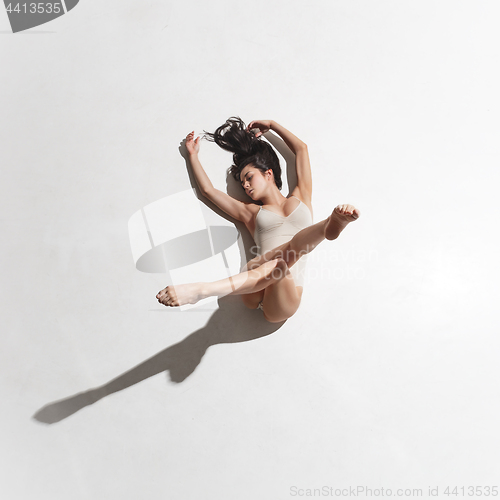 Image of Young beautiful dancer in beige dress dancing on gray background