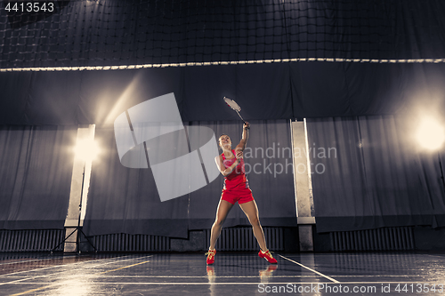 Image of Young woman playing badminton at gym