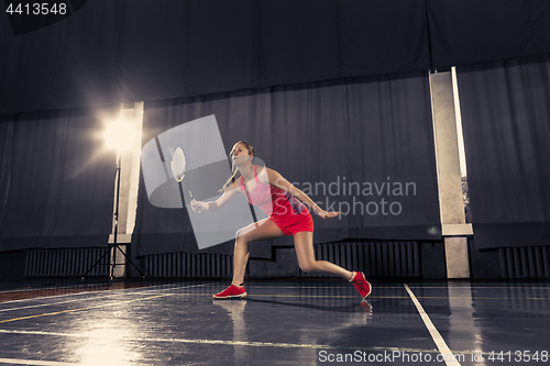 Image of Young woman playing badminton at gym