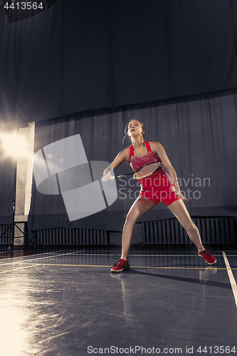 Image of Young woman playing badminton at gym