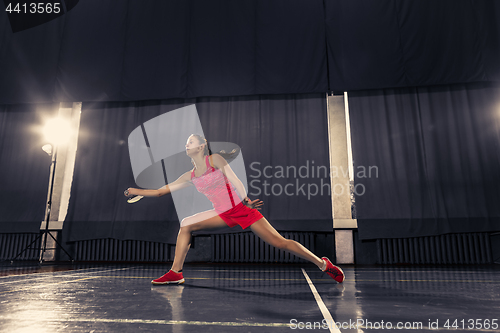 Image of Young woman playing badminton at gym