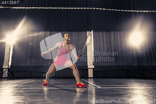 Image of Young woman playing badminton at gym