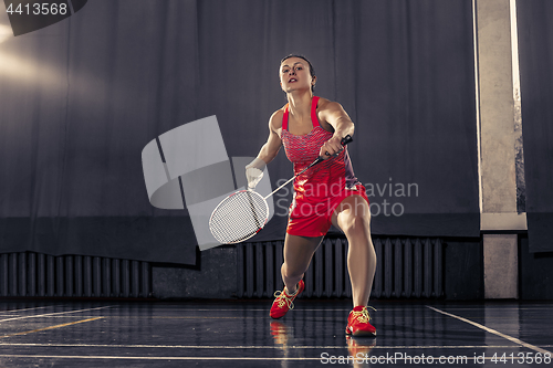 Image of Young woman playing badminton at gym