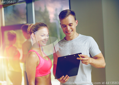 Image of smiling young woman with personal trainer in gym