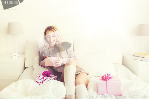 Image of happy young woman with gift boxes in bed at home