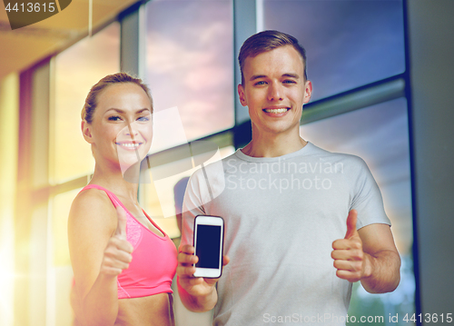 Image of smiling young woman with personal trainer in gym