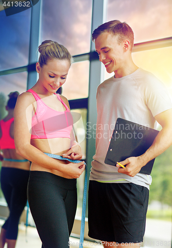 Image of smiling young woman with personal trainer in gym