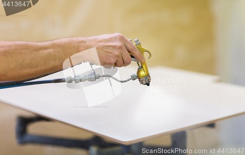 Image of worker hand sprays urethane finish to board