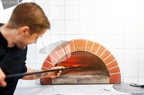 Image of man with peel placing pizza to oven at pizzeria