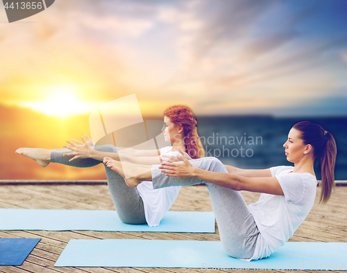 Image of women doing yoga half-boat pose outdoors