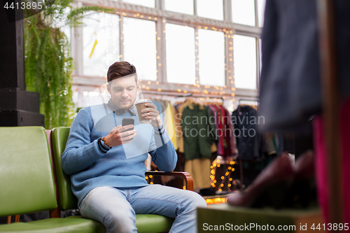 Image of man with smartphone and coffee at clothing store