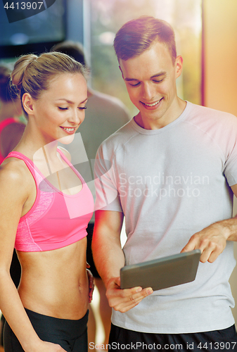 Image of smiling young woman with personal trainer in gym