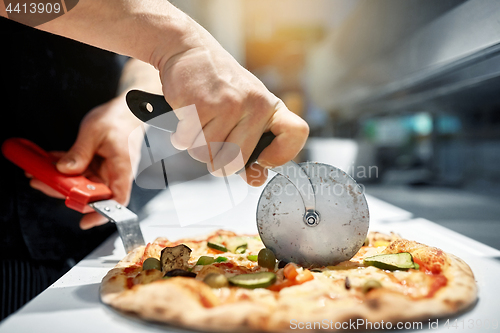 Image of cook cutting pizza to pieces at pizzeria