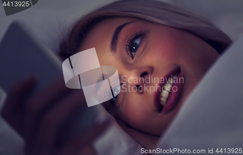 Image of young woman with smartphone in bed at night