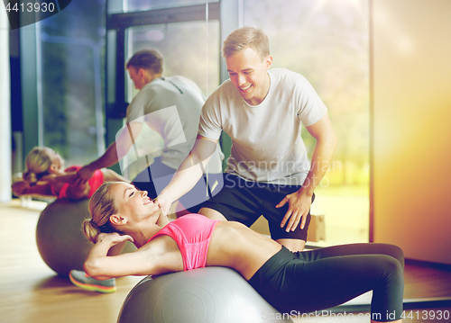 Image of smiling young woman with personal trainer in gym