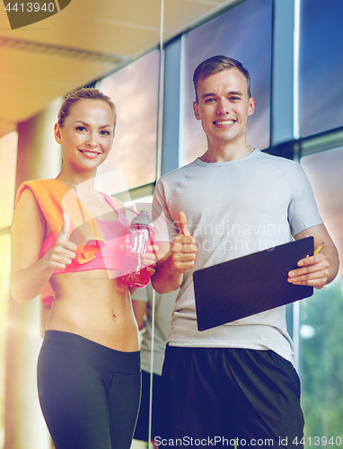 Image of smiling young woman with personal trainer in gym