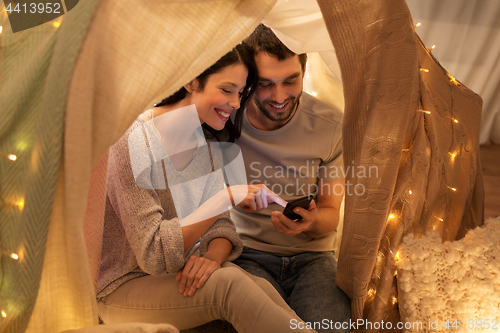 Image of happy couple with smartphone in kids tent at home