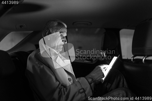 Image of Businessman with a digital tablet sitting in the back seat of a car