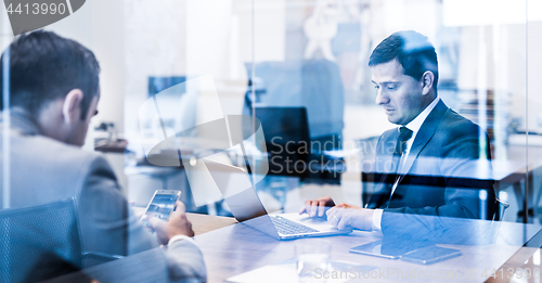 Image of Two young businessmen using laptop computer at business meeting.