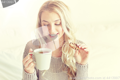 Image of happy woman with tea and cookies in bed at home