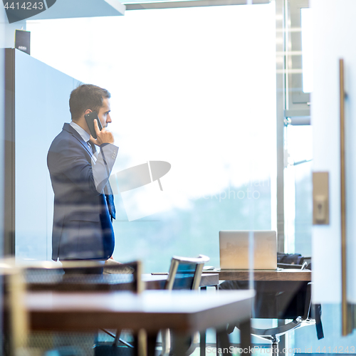 Image of Businessman talking on a mobile phone while looking through window.